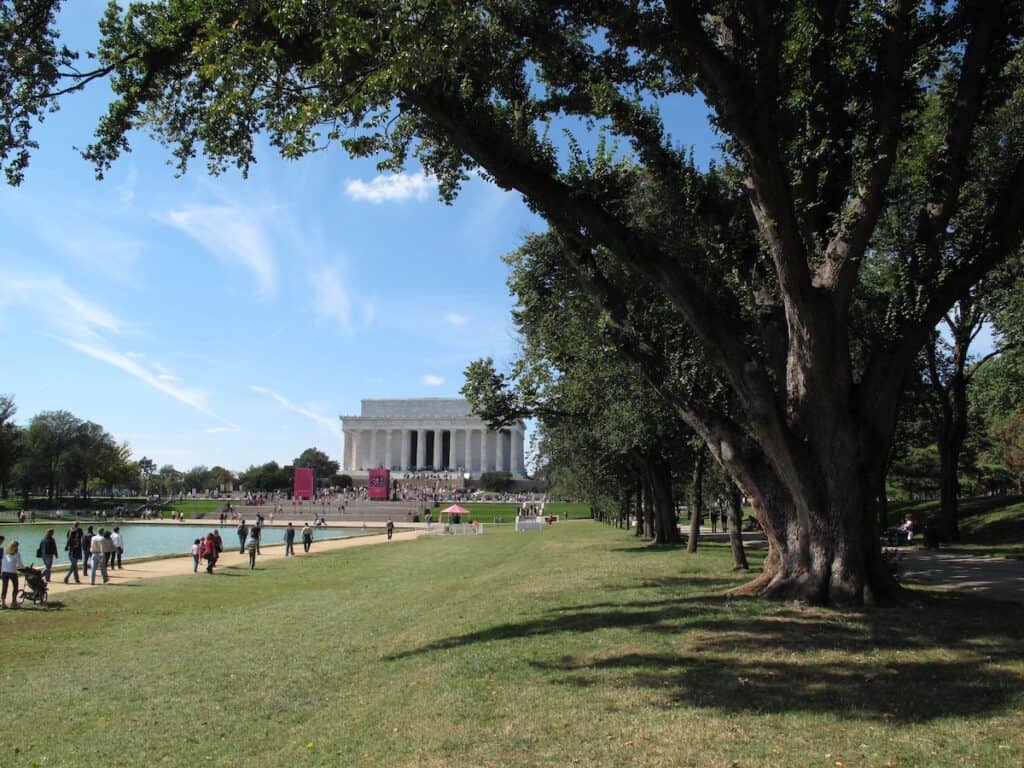 Serene park with Lincoln Memorial in the background, lush trees, and visitors enjoying tranquility. Peaceful outdoor scene featuring Lincoln Memorial and shaded trees in a tranquil park setting.